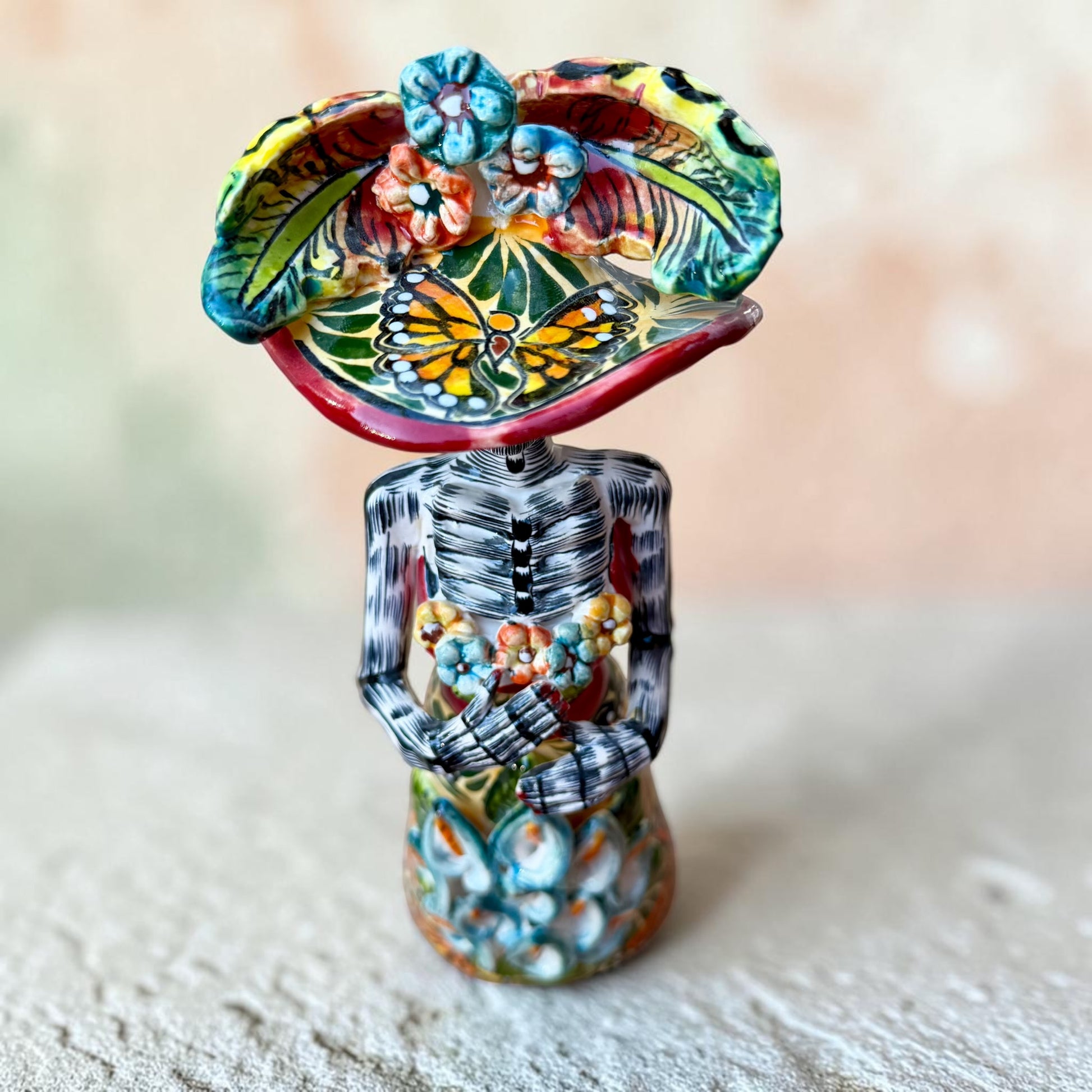 Mexican catrina talavera doll with calla lilies on the front of her dress. wearing a colorful dress with a big feathered hat.   Top view of doll.