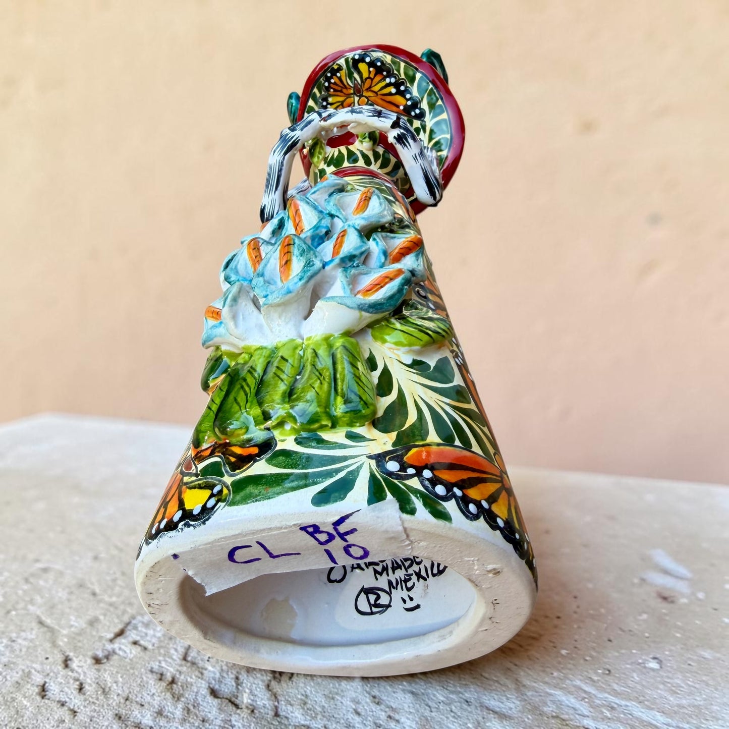 Mexican catrina talavera doll with calla lilies on the front of her dress. wearing a colorful dress with a big feathered hat.   Bottom view of doll showing signature.