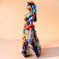 A colorful hand-painted Day of the Dead (Día de los Muertos) ceramic figurine of a  ballerina, decorated with vibrant floral patterns and a white skull head with braided hair, set against a solid peach background. Right side view of the lady showing her hand.
