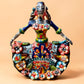A colorful hand-painted Day of the Dead (Día de los Muertos) ceramic figurine of a  ballerina, decorated with vibrant floral patterns and a white skull head with braided hair, set against a solid peach background.