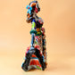 A colorful hand-painted Day of the Dead (Día de los Muertos) ceramic figurine of a  ballerina, decorated with vibrant floral patterns and a white skull head with braided hair, set against a solid peach background. Left side view of ballerina catrina doll.