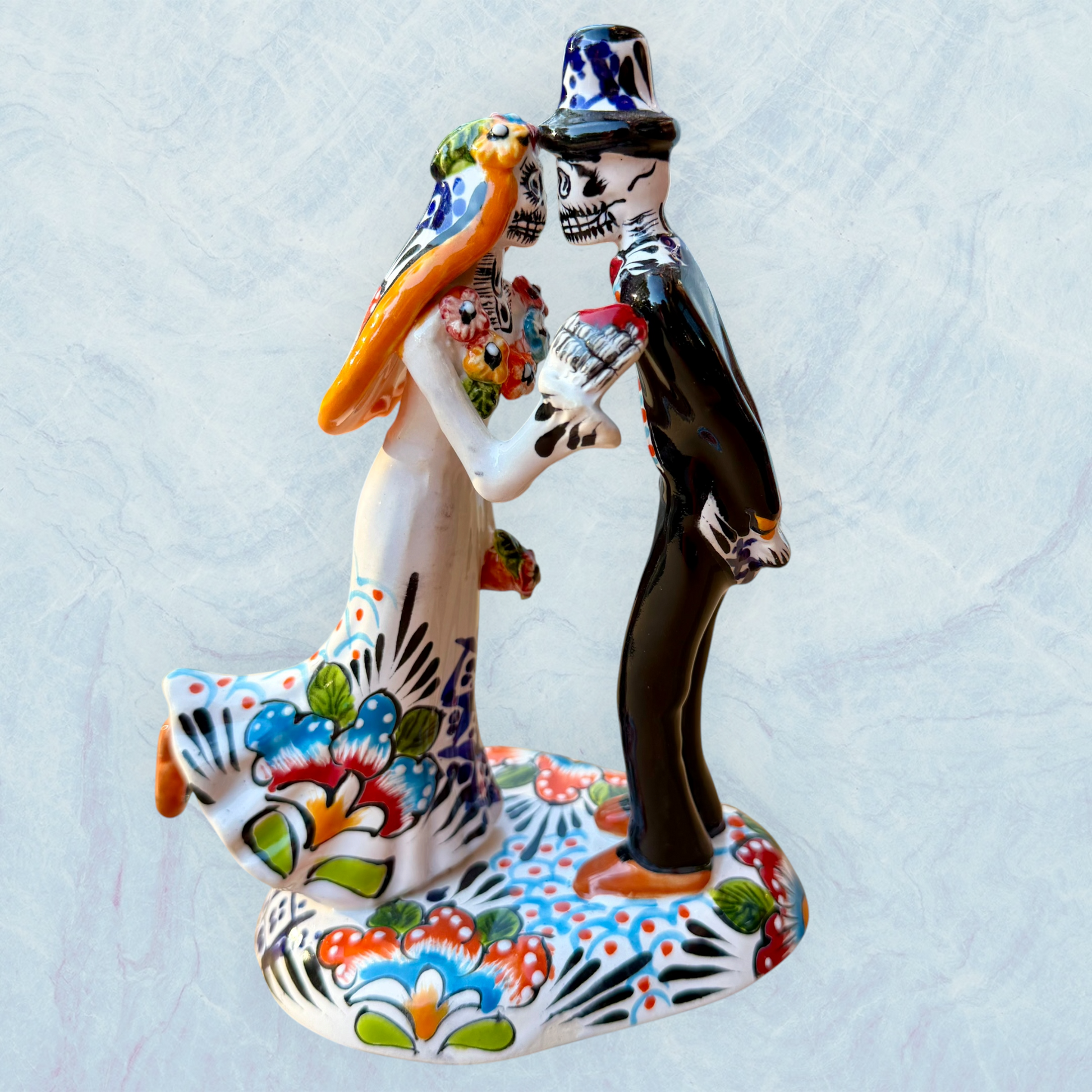 A hand-painted ceramic Day of the Dead figurine of a dancing skeleton couple, featuring a bride and groom with vibrant multicolor floral patterns on a white background.