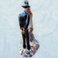 A hand-painted ceramic Day of the Dead figurine of a dancing skeleton couple, featuring a bride and groom with vibrant multicolor floral patterns on a white background.  side view focusing on the groom.