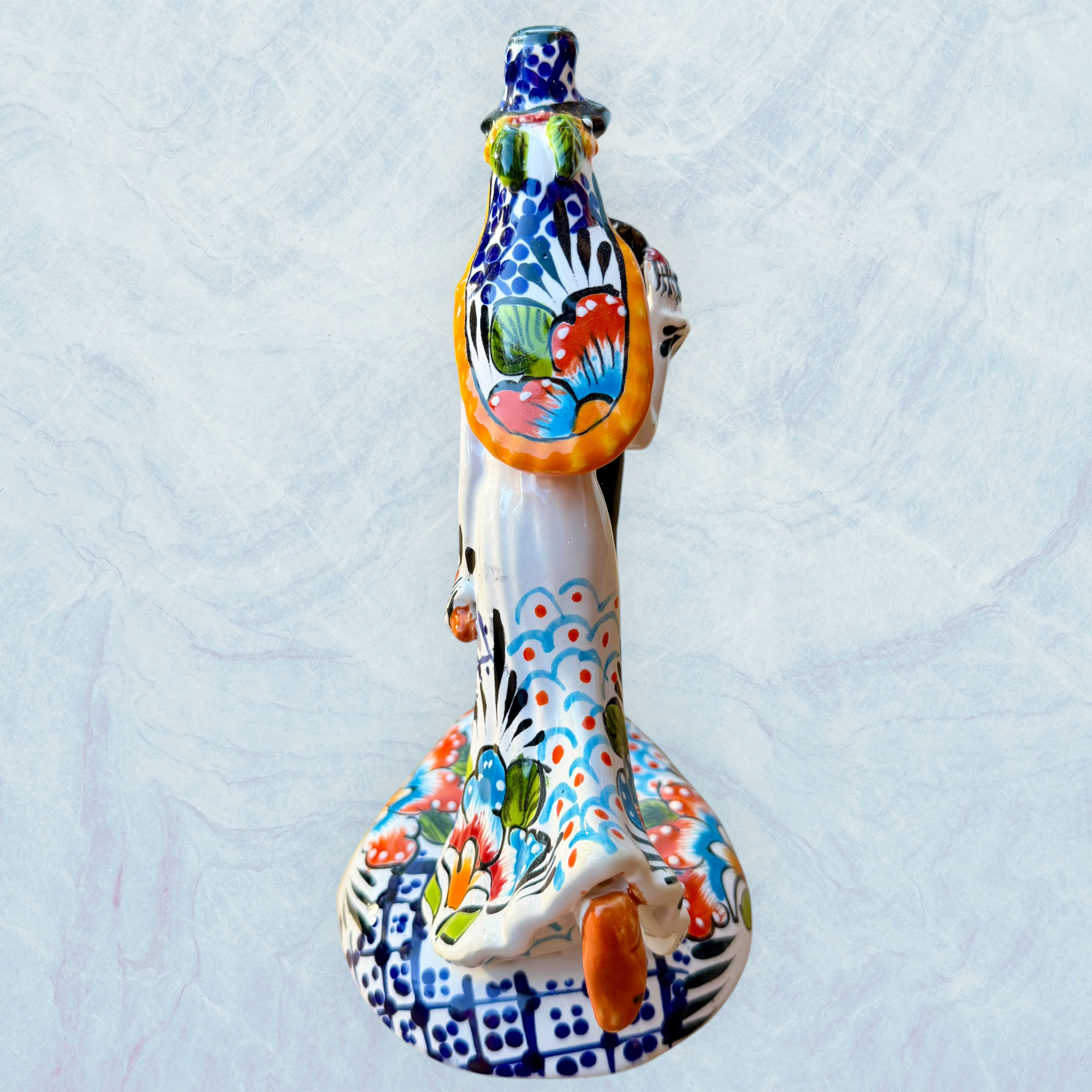 A hand-painted ceramic Day of the Dead figurine of a dancing skeleton couple, featuring a bride and groom with vibrant multicolor floral patterns on a white background. Side view featuring the brides dress and veil.