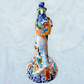 A hand-painted ceramic Day of the Dead figurine of a dancing skeleton couple, featuring a bride and groom with vibrant multicolor floral patterns on a white background. Side view featuring the brides dress and veil.