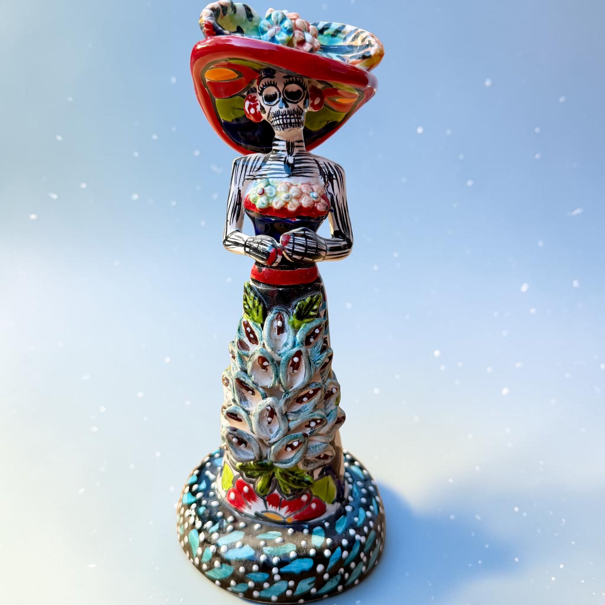 Mexican Catrina Doll made out of Talavera with Calla Lillies on the front of her dress.  Colorful pieces and a big feathered hat and a big toothy smile.