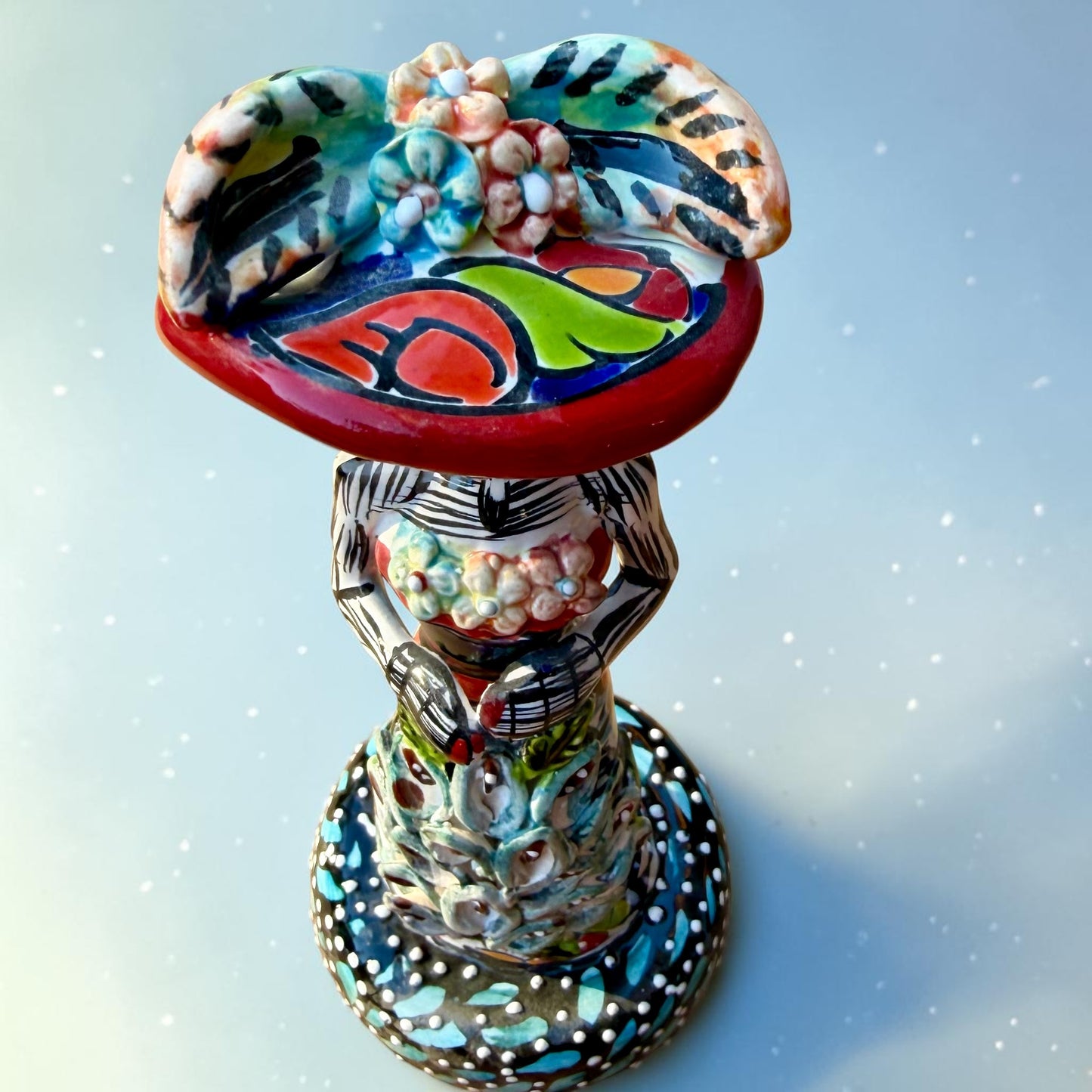 Mexican Catrina Doll made out of Talavera with Calla Lillies on the front of her dress.  Colorful pieces and a big feathered hat and a big toothy smile. Top view showing hat.