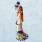 A decorative ceramic Day of the Dead wedding couple figurine featuring a black-and-white skeleton groom in a suit and hat with a butterfly patterned hat, and a white bride with orange hair in a floral gown with butterflies holding a bouquet, set against a light textured background. This is the right side view.